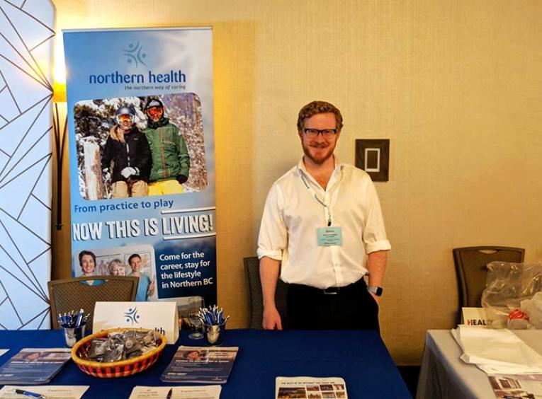 A man stands smiling in the Northern Health recruitment booth