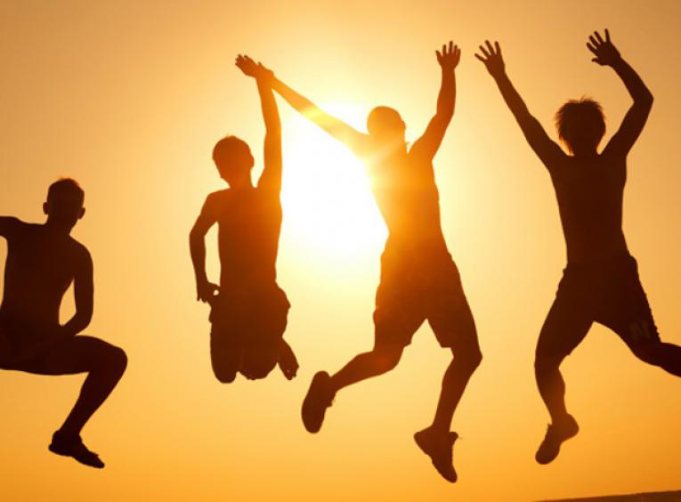 Silhouette of four people jumping together against setting sun behind