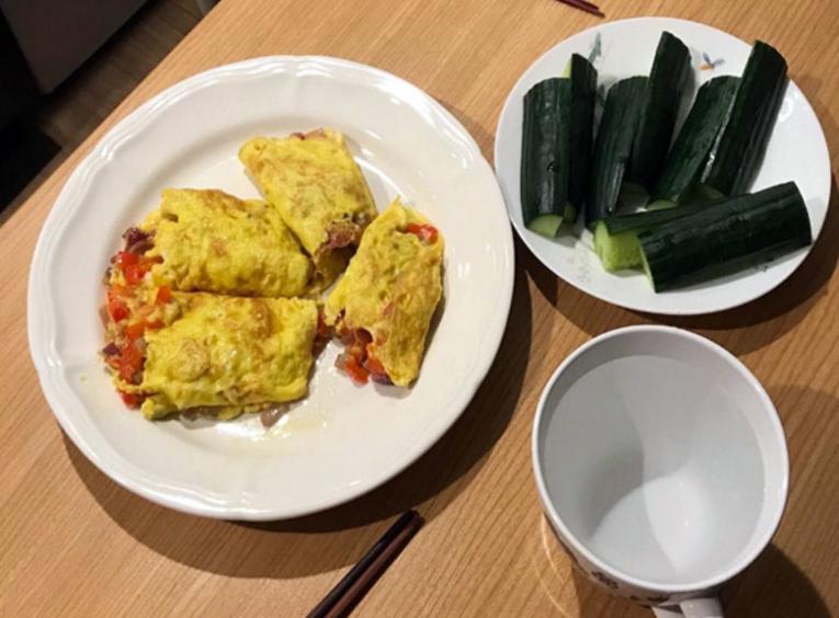 A plate of cucumbers, a omelette dish, and a glass of water are pictured.