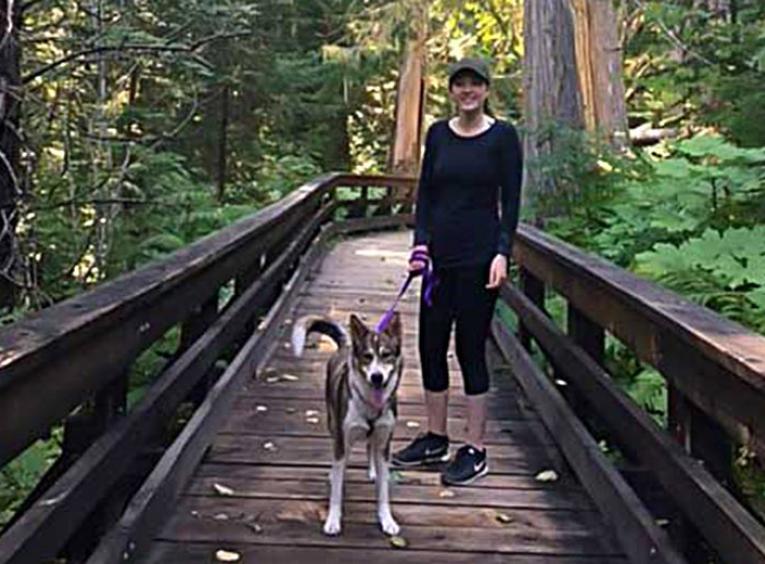 Jaymee webster on a bridge in the woods with her dog.