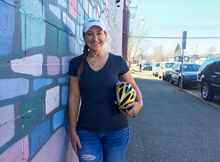 Woman standing in street holding cycling helmet.