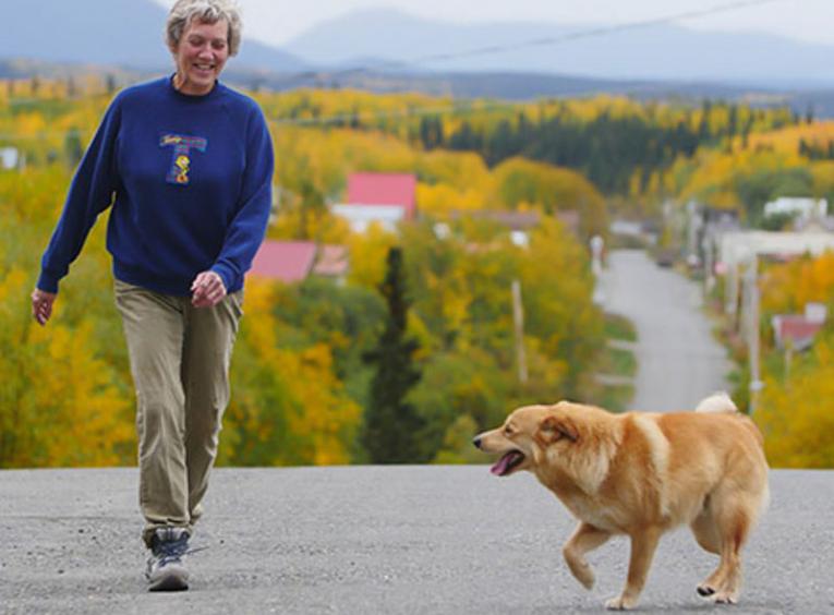 Woman walking with dog on asphalt road during fall