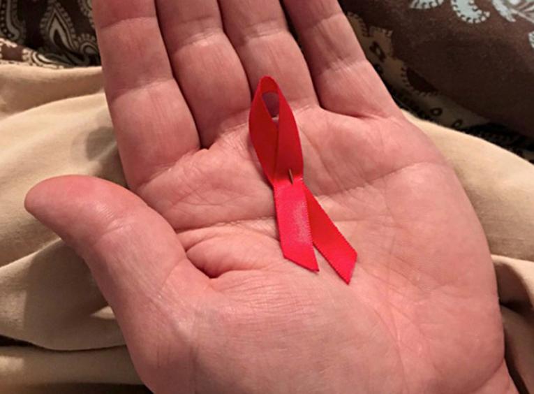 Small red AIDS ribbon in the palm of someone's hand.
