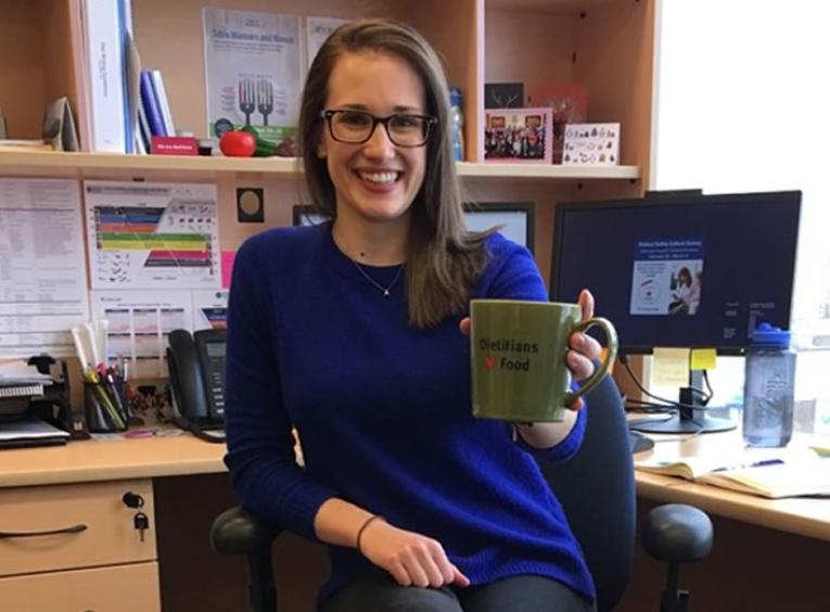 Allie Stephen sitting at her desk with a mug that says "Dietitians (heart) food."