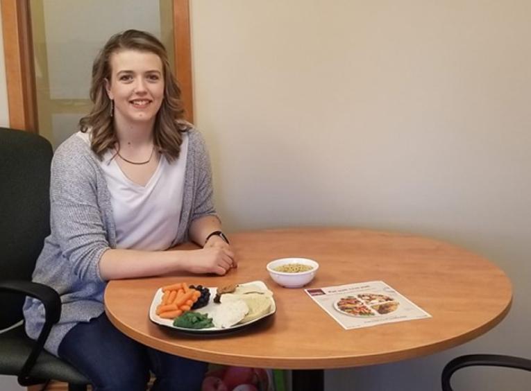 Amelia Gallant sitting at a table with a balanced meal and Canada's Food Guide.
