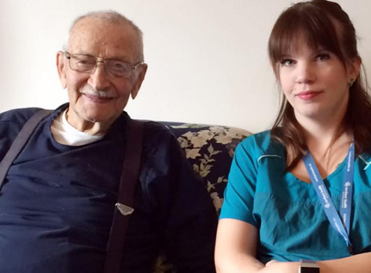 An elderly man and a young woman sit on a couch.