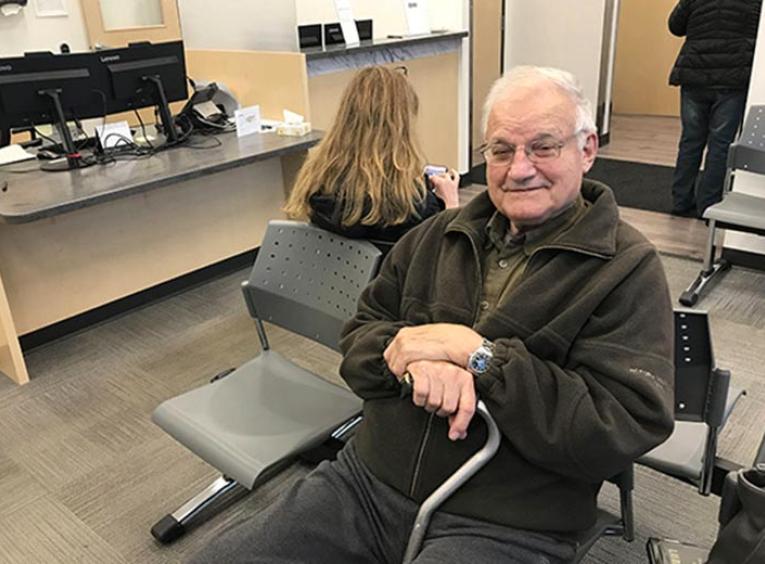 A man with a cane sits on a chair in the waiting room.