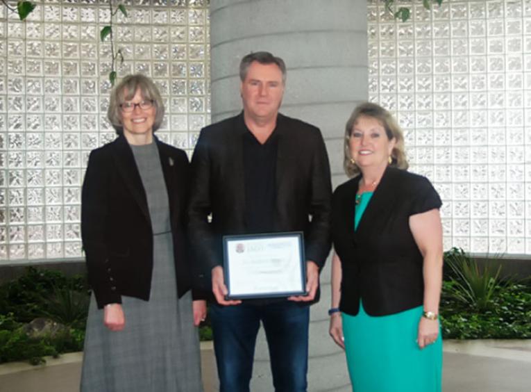 A man standing between two women holding a plaque award.