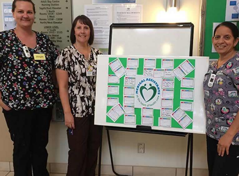 Care aides standing and smiling with thank you board .