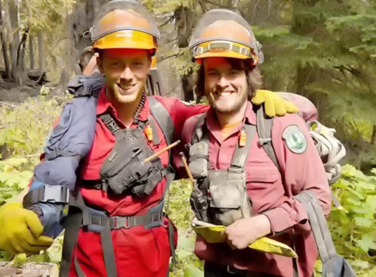 Two young men standing in a forest with their forest firefighting gear on.