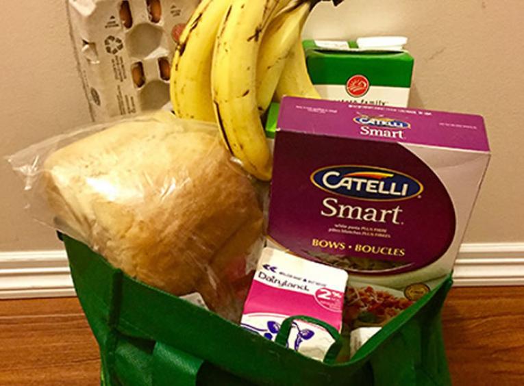 Grocery bag with bananas, eggs, bread, pasta and milk.