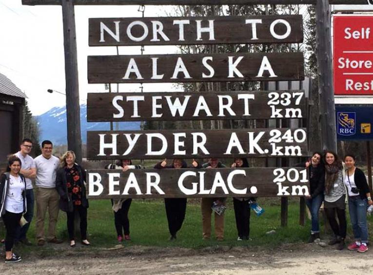 Group standing below a big wooden sign showing towns.