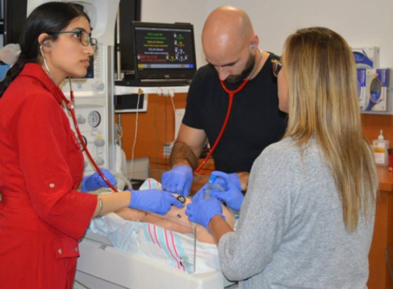 Three medical students taking a simulated learning session with a baby simulator.