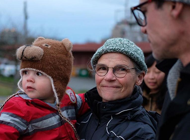 A woman outside holding a toddler boy in a bear toque.