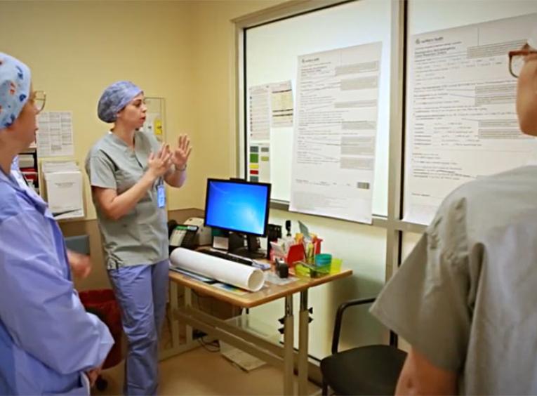 Three women wearing hospital scrubs looking at a whiteboard.