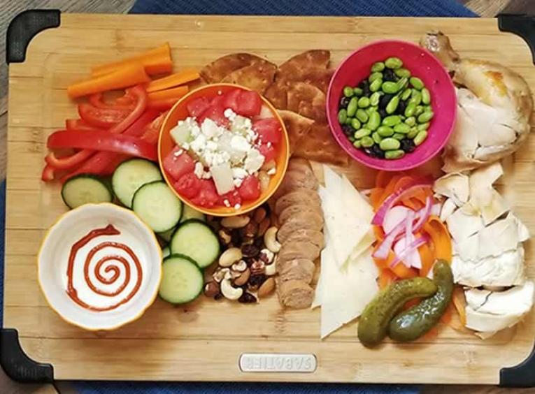 Snack foods on a board including meat, cheese & pickles.