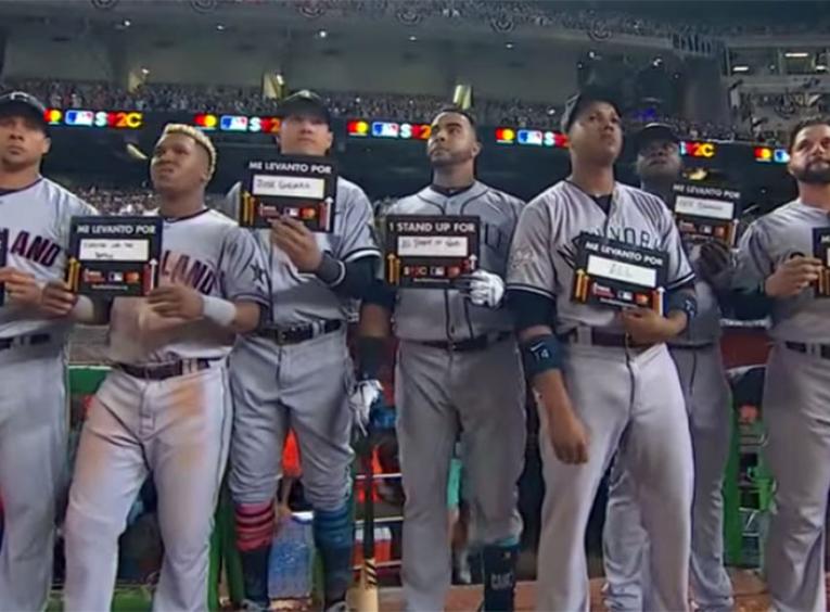 MLB Baseball players in a row during game night while holding stand up to cancer placards.