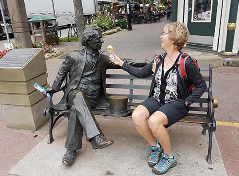 Susan Knoll sitting on a bench with a statue, eating ice cream. 