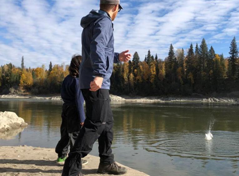 A man and child throwing rocks into a lake.