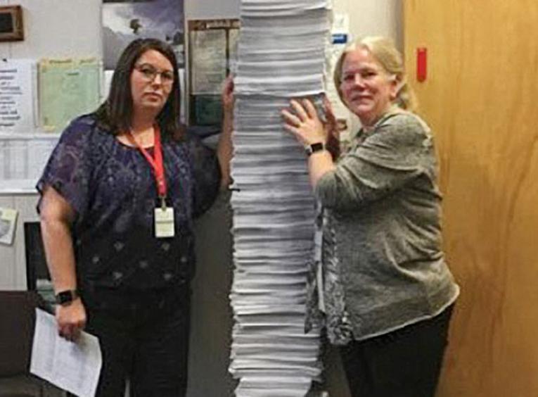 Two women standing with a tall stack of chart copies between them.