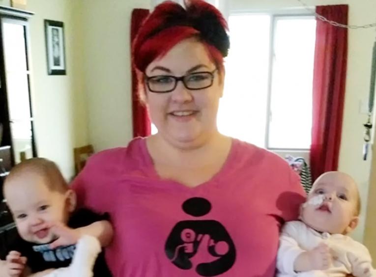 Woman in a pink shirt holding a baby in each arm.