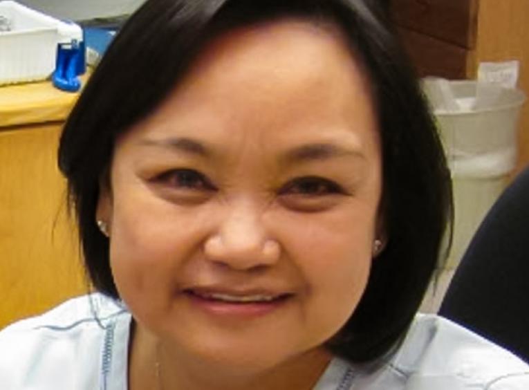 Woman with dark hair and wearing a nurses uniform smiling.