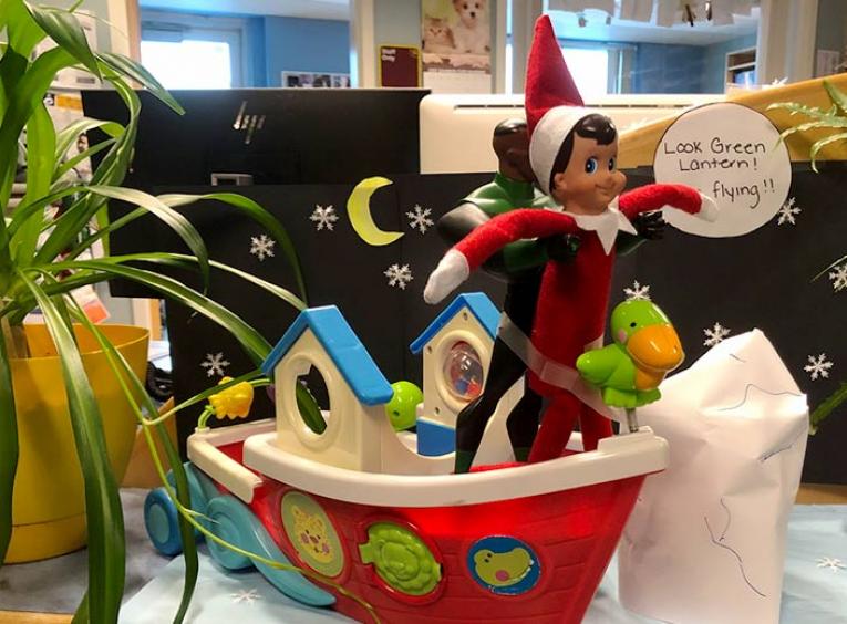 The elf on the shelf is held up by a toy version of the super hero Green Lantern, reenacting a scene from the movie Titanic. 