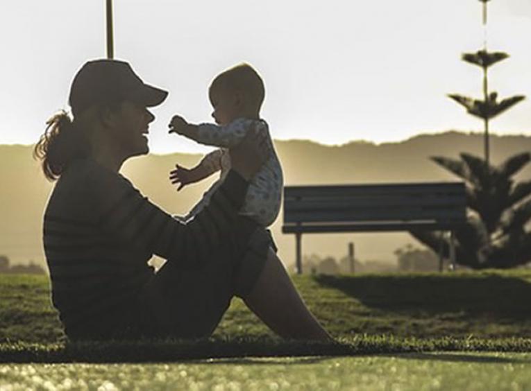 Woman sitting on the ground outside holding a baby.