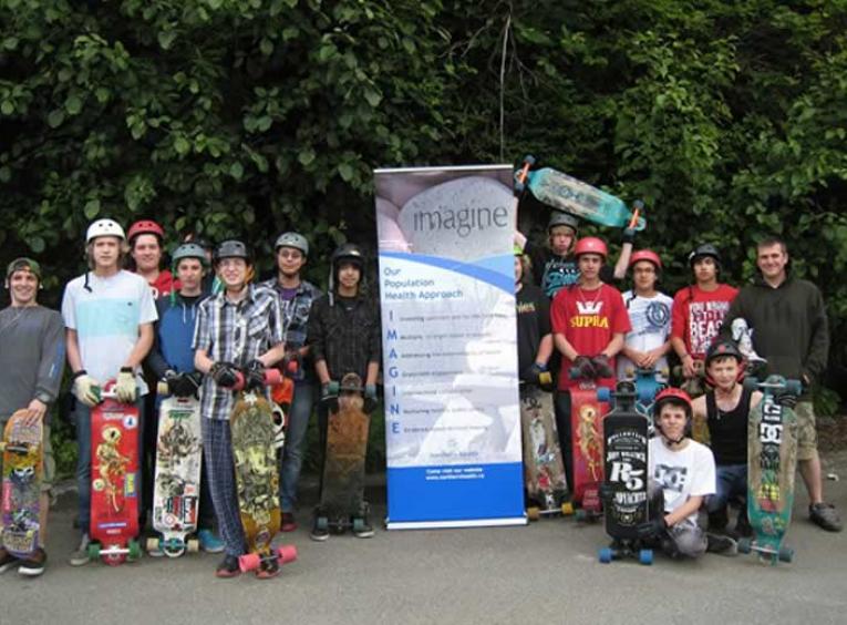 Large group of youth standing with skateboards and wearing helmuts.