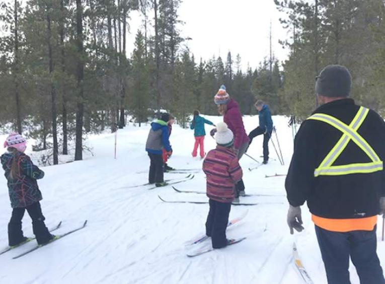 Group of kids, wearing bright jackets and hats, cross country skiing.