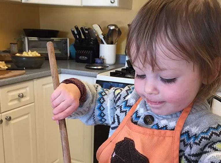 Toddler holding a wooden mixing spoon over a bowl full of oats.