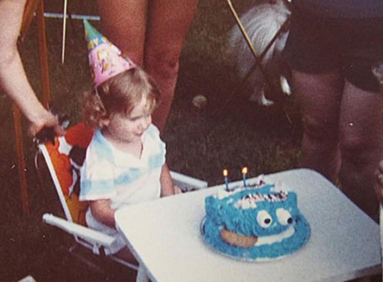 Toddler wearing birthday hat and blue cake.