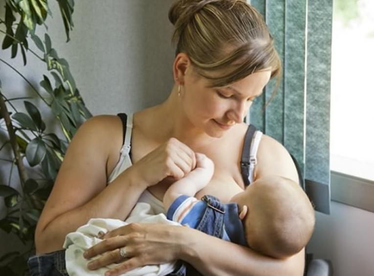 Woman with hair pulled up breastfeeding her baby.
