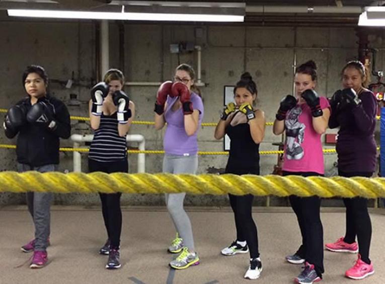 Group of 5 female teens in a boxing ring wearing boxing gloves.