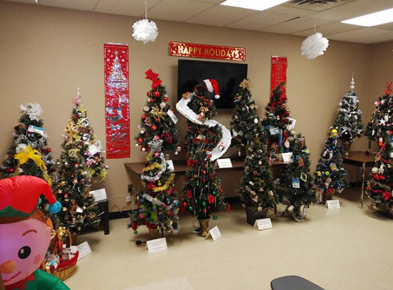 A line up of small, decorated Christmas trees in a large room decorated for Christmas.