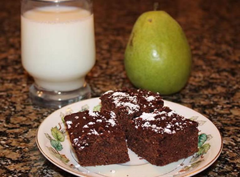 Plate with 3 brownies beside an pear and a glass of milk.