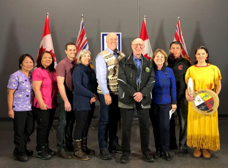 A group of 5 women and 4 men stand on stage smiling. 