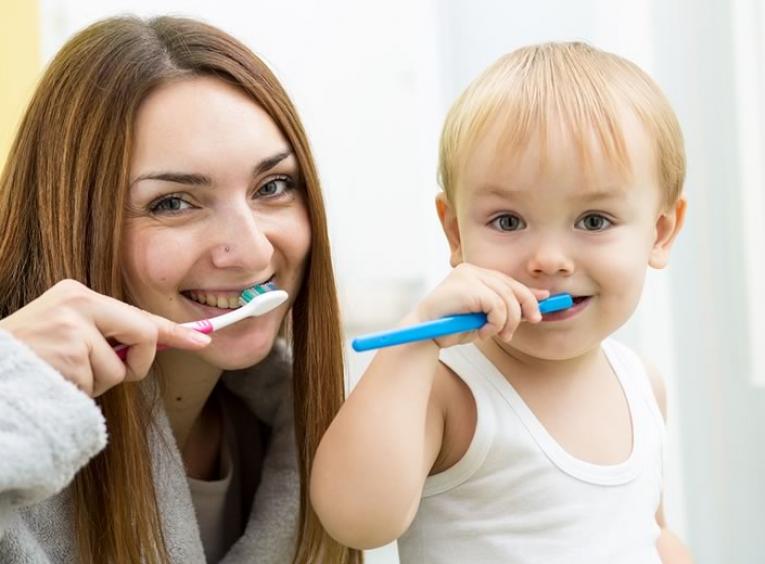 Woman with long hair and toddler both brushing their teeth.
