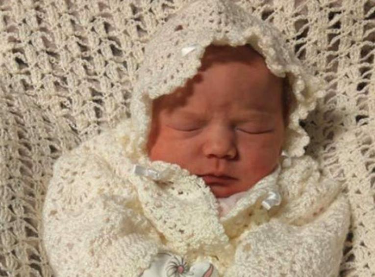 A newborn baby laying on a beige blanket.