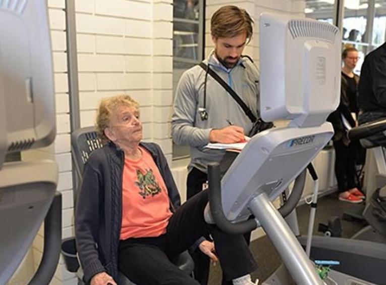 Patient on exercise bicycle monitored by physiotherapist.