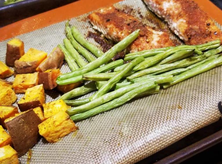 A sheet pan of cooked yams, green beans, and salmon.