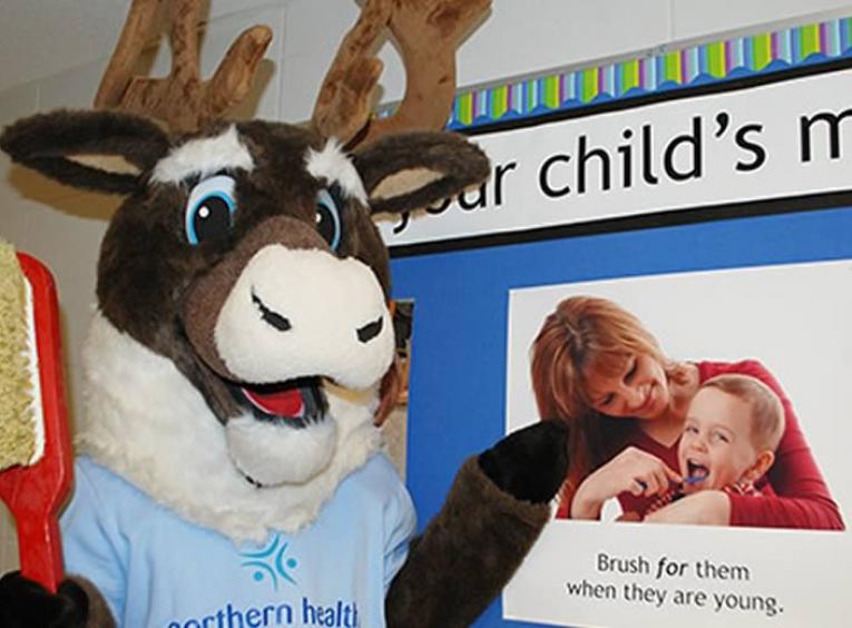 Spirit the caribou mascot holding a giant red toothbrushin front of poster