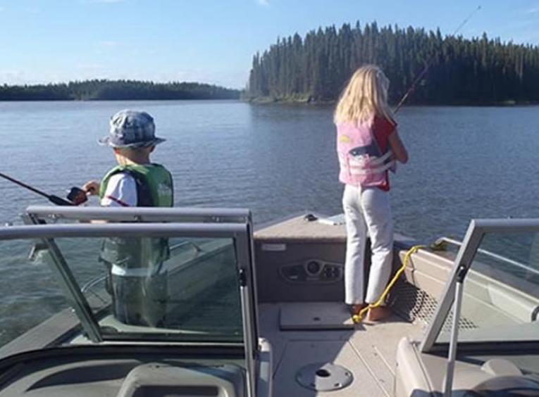 A young boy and girl standing at the front of a boat fishing.