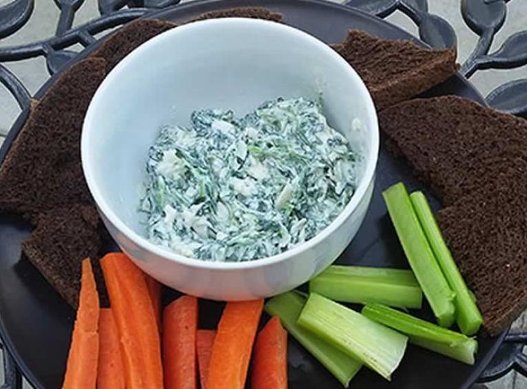 Spinich dip in a bowl surrounded by carrots, celery and dark bread.