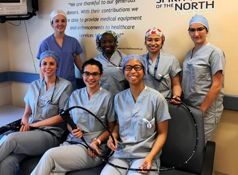 Seven nurses smile into the camera, holding a pediatric colonoscope.