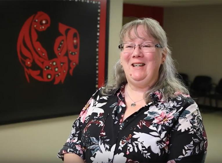 A woman sits in a room with Indigenous artwork in the background.
