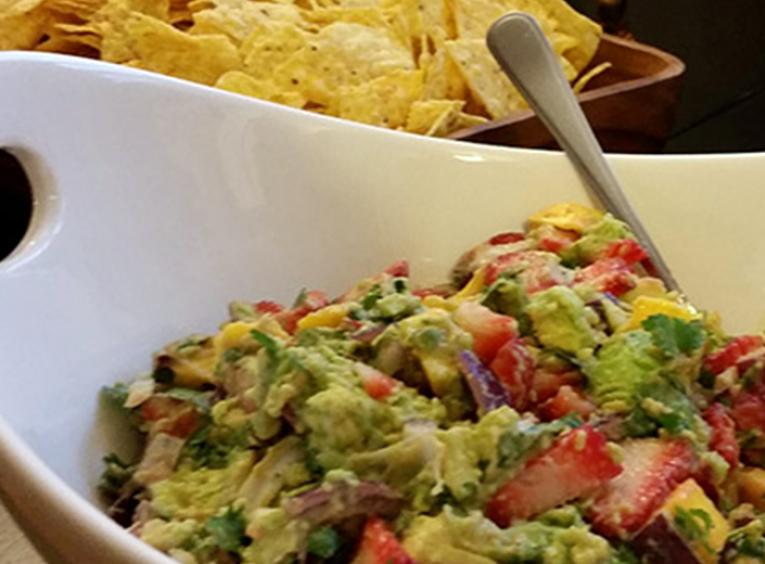 Strawberry mango guacamole in a white bowl, with spoon, and chips in background