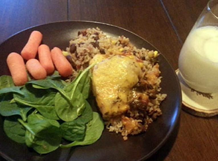 Chicken casserole with spinach, carrots and wild rice on a plate, served with a glass of milk