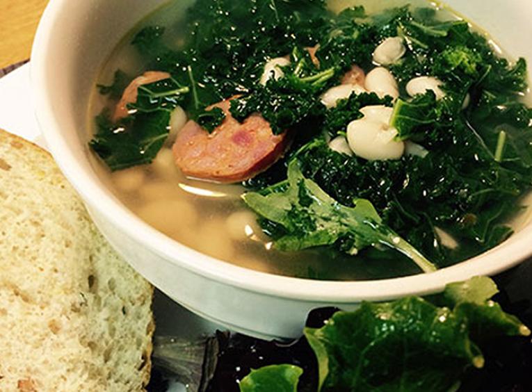Bowl of kale, white bean and sausage soup served with bread and salad