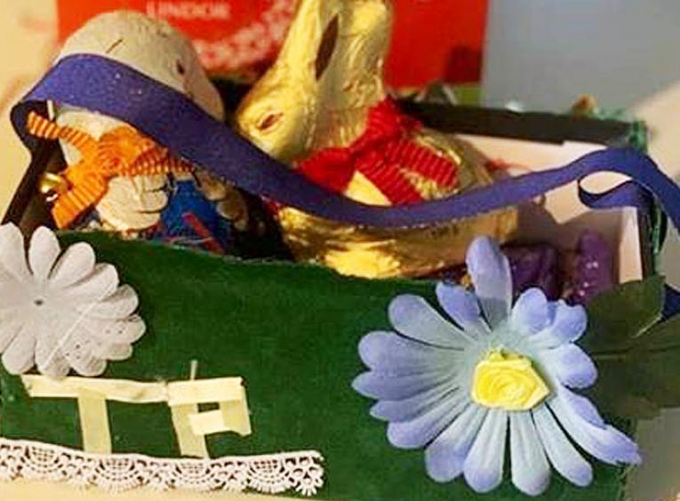 A green homemade Easter basket has the initials TP on it, as well as decorative blue and pink flowers.